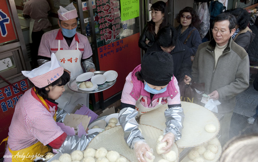 Steam rises from freshly cooked king dumplings or mandu as a crowd of hungry people with cash in their hand wait to buy the famous hot dumplings. Namdaemun Market, Seoul, South Korea