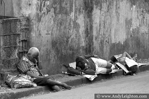 Three poor people rest and sleep on cardboard on the edge of the road. Cebu City, Philippines