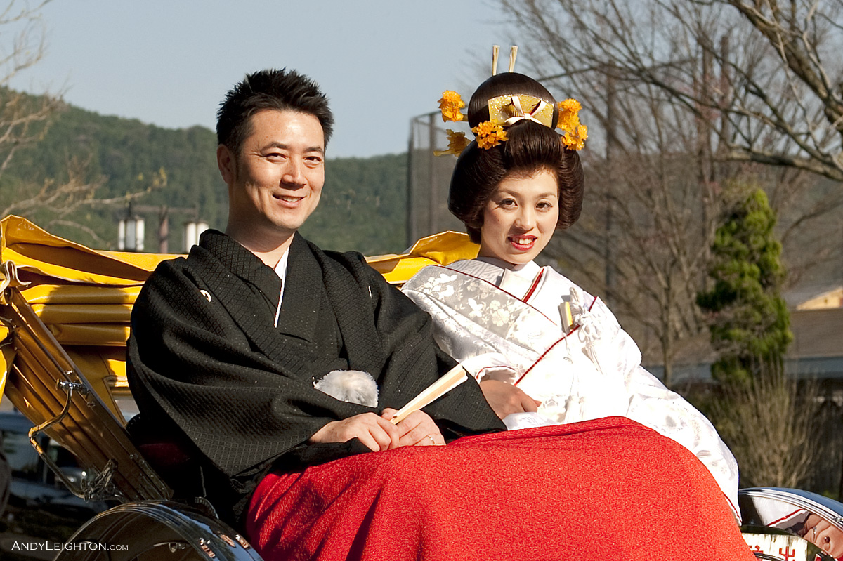 A Japanese bride and groom dressed in tradition wedding ceremony costume ride along the footpath in a 'jinrikisha' or rickshaw. Kyoto, Japan