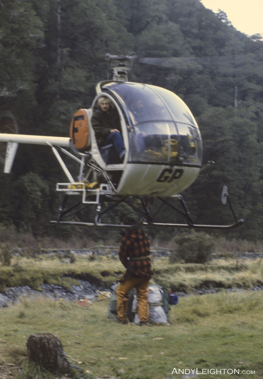 Andy Nolan unhooking packs and supplies from under the hovering Hughes 300 helicopter. Trent River, Westland, New Zealand. HGP, Tom Trevors (pilot), Andy Nolan (shooter), Garry Turnbull, Pete Gurden