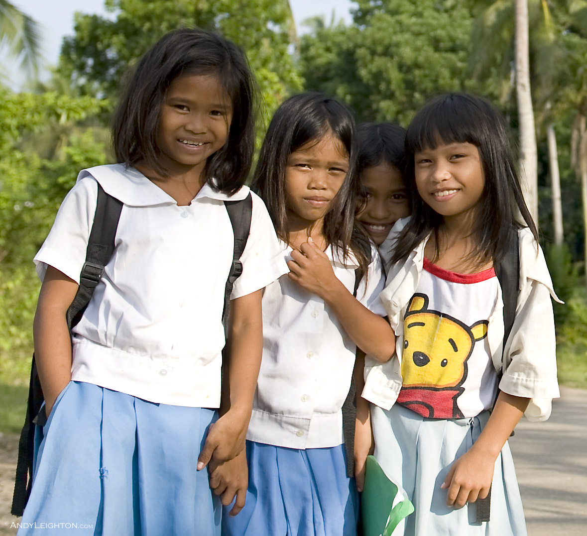 Four school girls smile for the camera with a background of coconut trees on a country road. Panglao Island, Philippines